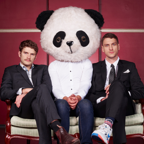 Image is of Carlo Ritchie (left) and Steen Raskopoulos (right). Both men are wearing suits and sitting next to a Panda Mascot.