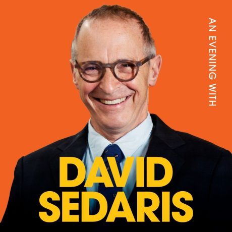 David Sedaris smiles wearing a suit. He's against an orange background. The Words 'An Evening With David Sedaris' appear on the image.