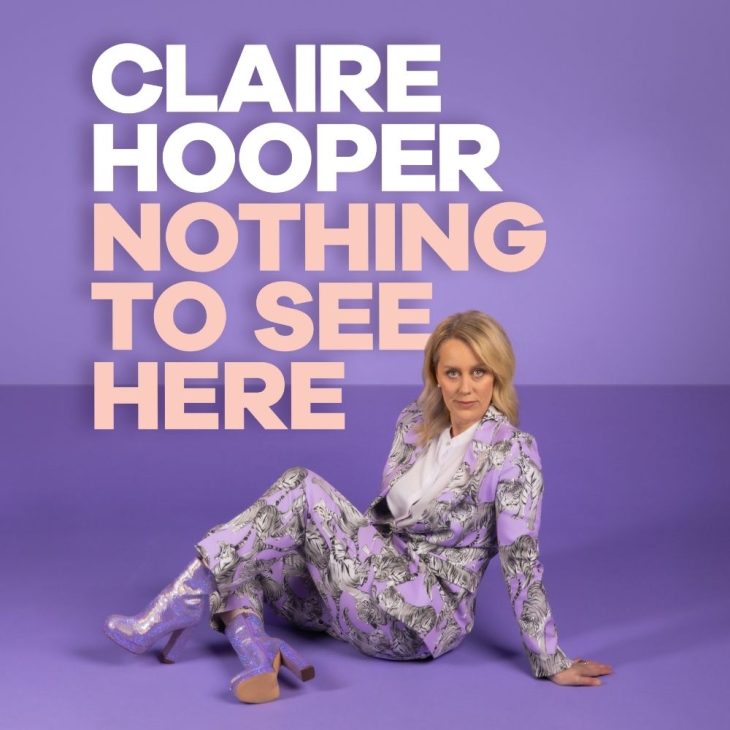 Claire Hooper poses in front of a purple backdrop. She wears a purple floral suit and sparkly purple boots.