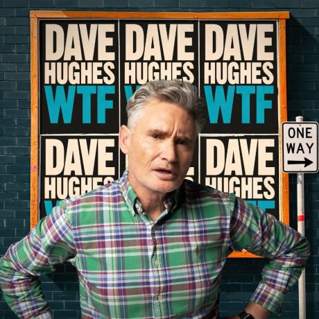 Dave Hughes stands in front of a brick wall. The wall is covered in posters that say 'Dave Hughes WTF'