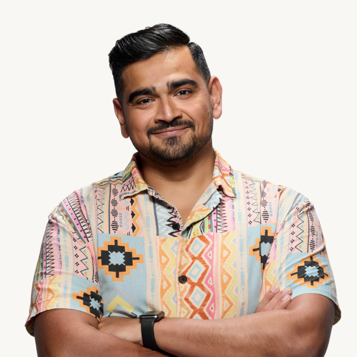 Dilruk Jayasinha smiles gently with his head tilted to his right. He wears a short-sleeved shirt with various patterns in many pastel colours. He has a neatly trimmed, short black bread and moustache and his black hair is combed back and parted on his left. The backdrop is off white.