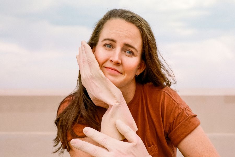 Comedian Zoë Coombs Marr looks at the camera. She wears huge novelty hands.