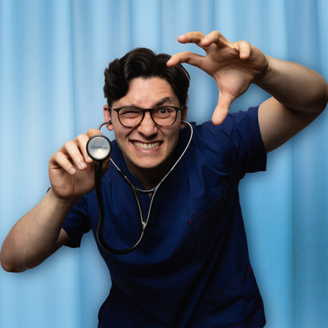 Noah Szto has short brown hair and black framed glasses. He is wearing navy blue hospital scrubs and a stethoscope. His left-hand lifts the stethoscope to the camera and his right hand is in the shape of a claw. He has an evil expression on his face.