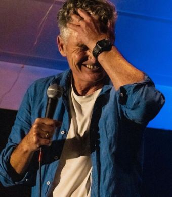 Image is of Dave Hughes performing stand up comedy