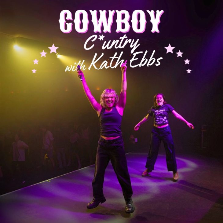 Kath ebbs is on a stage. Pink spotlight on them. They jump with a microphone in hand. People line dance in the background.