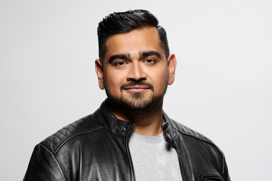 Image is of Dilruk Jayasinha. He is wearing a grey shirt and a black leather jacket. Dilruk has short dark hair and a dark beard. He is smiling into the camera lens.