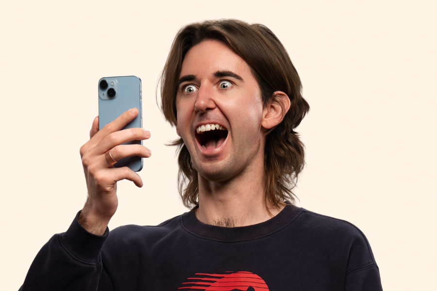 Image is Fergus Neal. Fergus has long brown hair and is wearing a dark sweatshirt. He is holding up an iPhone and looking into the screen with a surprised expression on his face. The image has been edited to look like Fergus is a cartoon