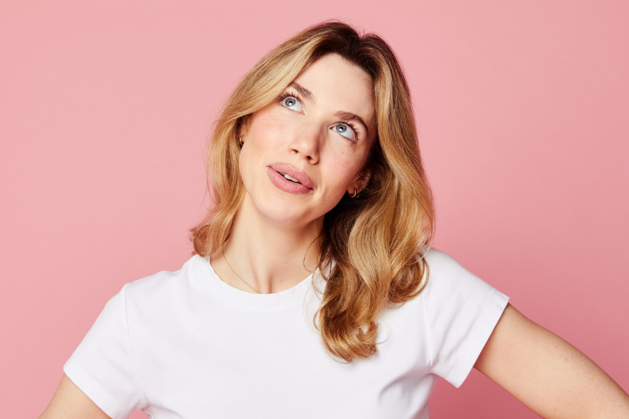 Image is of Tilly Oddy-Black. Tilly is wearing a white t-shirt and has long blonde hair. She is looking up and smiling.