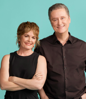 Image is of Sarah Kanowski and Richard Fidler standing side by side against a teal background, both smiling. Sarah has her arms crossed and wears a sleeveless black top, while Richard wears a black button-up shirt.