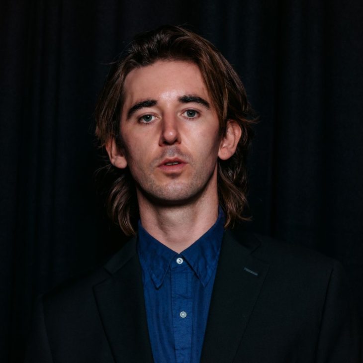 Fergus Neal wears a button up in front of dark backround.